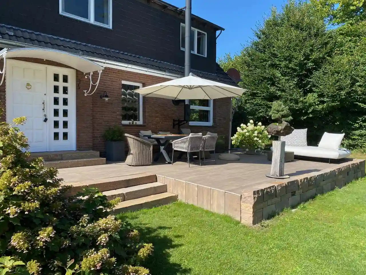 Terrasse mit Sitzgruppe und Sonnenschirm. Terrassenboden mit Keramikplatten in Holzoptik.